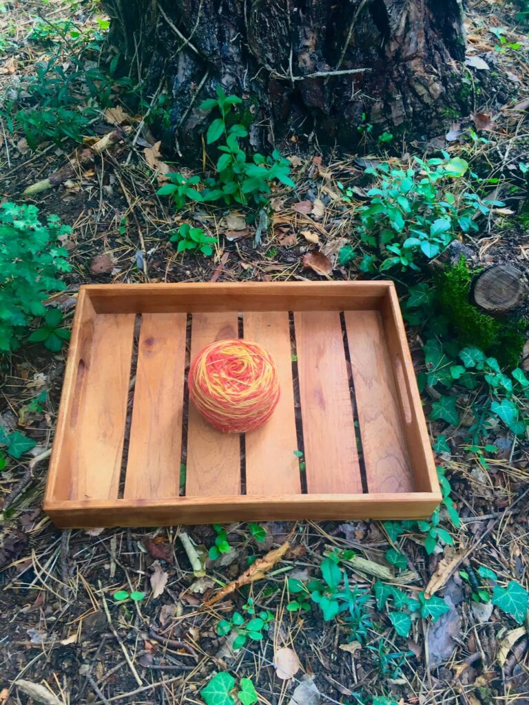 A skein naturally dyed with madder and onion is displayed in front of a tree