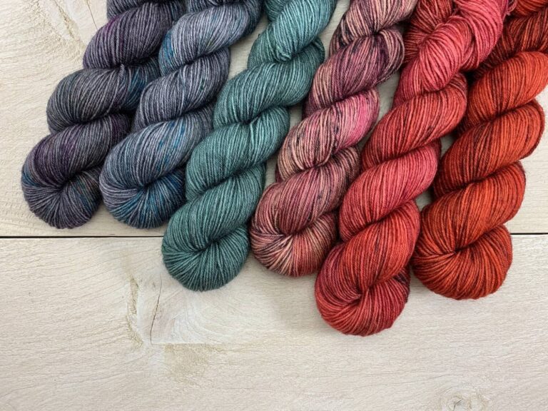 Six skeins of 50g BFL yarn in red, green and blue-grey colorways