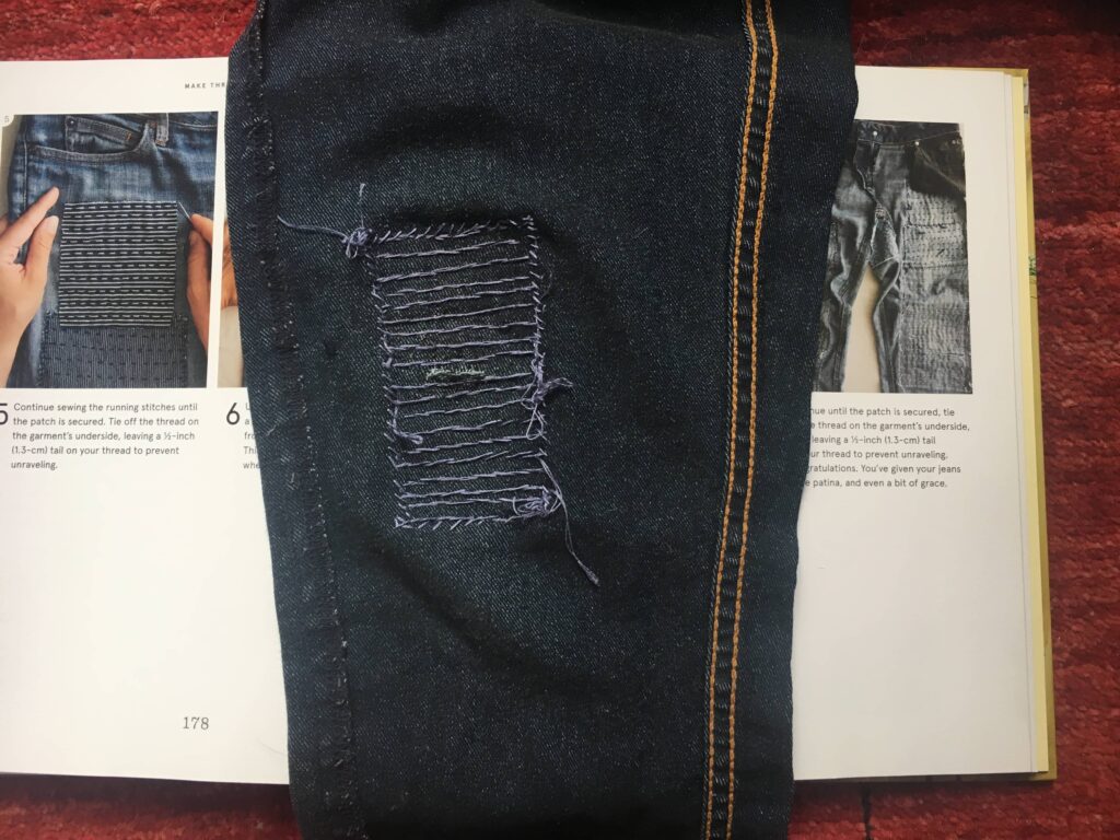 Jeans being mended and laying on top of the book Make Thrift Mend