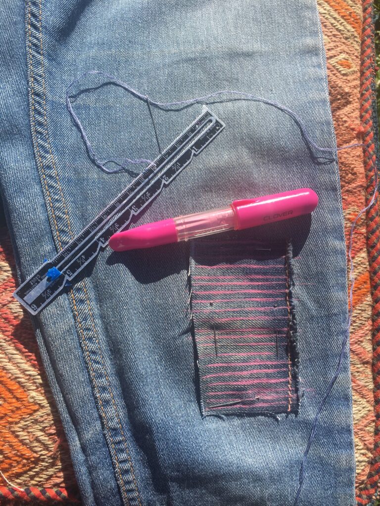 Mending jeans with a ruler and pink chalk to prepare the mending project