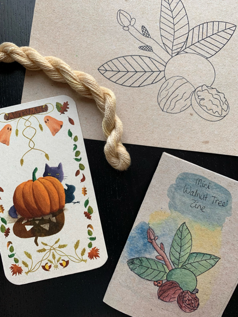 A close up of the naturally dyed embroidery thread andthe illustrated card with a pumpkin, a cat and a bird on it.