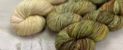 3 skeins of single ply yarn in green, brown and beige hues.
