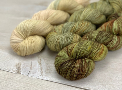 3 skeins of single ply yarn in green, brown and beige hues.